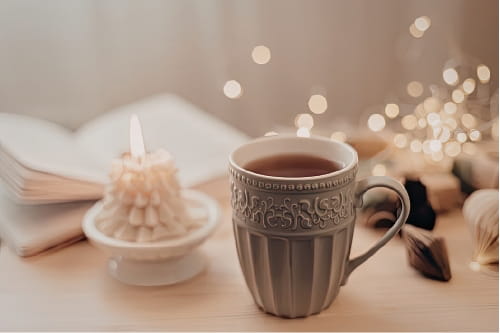Tasse Tee mit Kerze und Buch auf einem Tisch bei warmem Licht am Abend